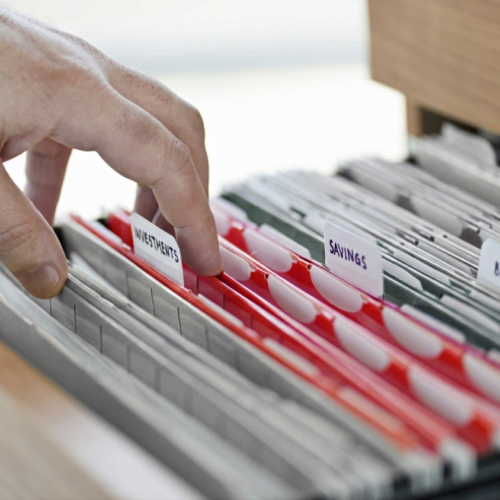 Person sorting organized business documents in a filing cabinet.